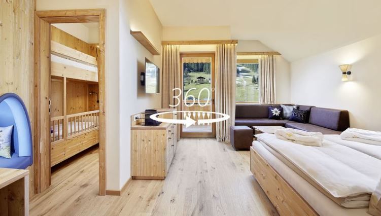 Helles Wohnzimmer mit Bett, Couch, Balkonzugang, links eine offene Tür mit Stockbett, mittig ein 360° Zeichen. Helles Wohnzimmer mit Bett, Couch, Balkonzugang, links eine offene Tür mit Stockbett, mittig ein 360° Zeichen.