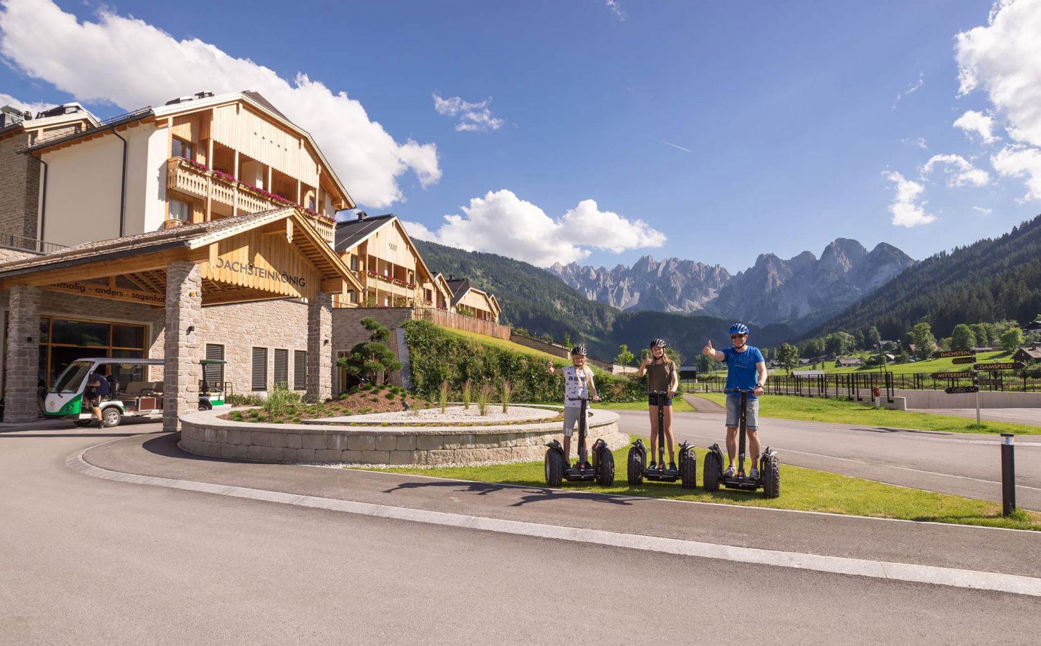 Drei Personen stehen mit Daumen hoch auf Segways, im Hintergrund das Dachsteinkönig Familux Resort. Drei Personen stehen mit Daumen hoch auf Segways, im Hintergrund das Dachsteinkönig Familux Resort.