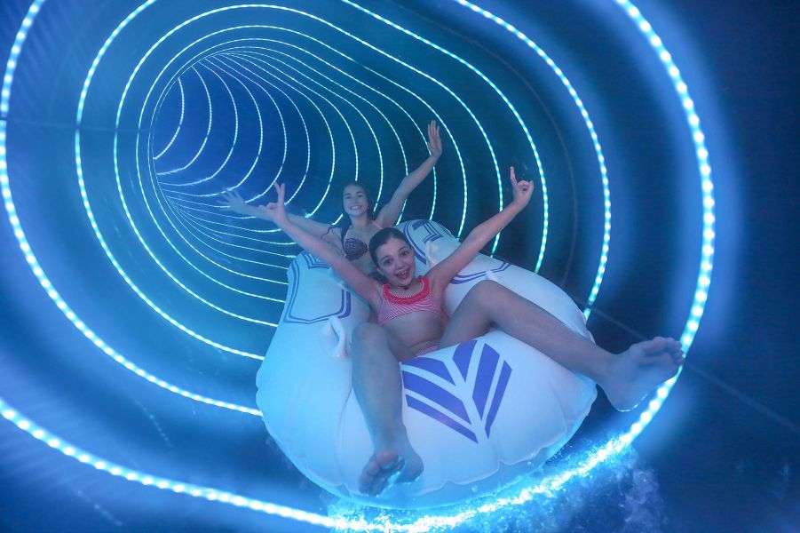 Dark blue, enclosed water slide with two girls on a tire. Dark blue, enclosed water slide with two girls on a tire.