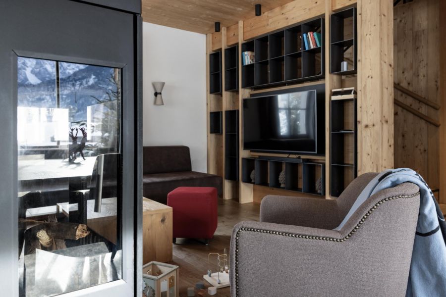 Gemütlicher Wohnraum mit Sessel vor einem Kamin, im Hintergrund eine Couch und ein TV an der Wand. Gemütlicher Wohnraum mit Sessel vor einem Kamin, im Hintergrund eine Couch und ein TV an der Wand.
