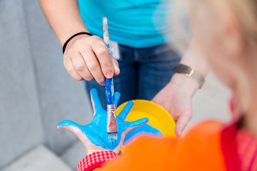Nahaufnahme einer Kinderhand, die gerade von einem Pinsel hellblau angemalt wird. Nahaufnahme einer Kinderhand, die gerade von einem Pinsel hellblau angemalt wird.